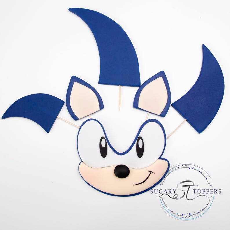 May include: A cartoon character face with blue spikes and ears, a white face, and a black nose and eyes. The character's face is smiling. The image includes the text "Sugary Toppers" in a circular design.