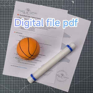 May include: An orange basketball cake topper next to a white rolling pin with blue bands, and printed instructions. The text "Digital file pdf" is overlaid on the image. The background is a gray cutting mat.