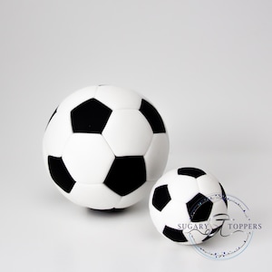 Pu&ograve; includere: Due decorazioni sferiche a forma di pallone da calcio con il classico motivo nero e bianco a pentagoni ed esagoni. Il pallone pi&ugrave; grande &egrave; posizionato a sinistra, mentre quello pi&ugrave; piccolo &egrave; a destra e riporta la scritta Sugary Toppers.