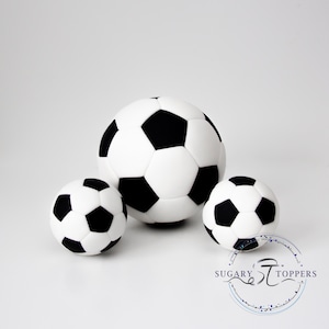 Pu&ograve; includere: Tre decorazioni sferiche a forma di pallone da calcio con il classico motivo a pentagoni ed esagoni bianchi e neri. Il pallone centrale &egrave; pi&ugrave; grande dei due laterali. &Egrave; visibile un logo circolare con il testo SUGARY TOPPERS.