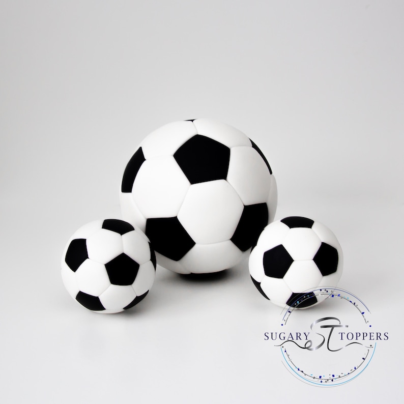 Pu&ograve; includere: Tre decorazioni sferiche a forma di pallone da calcio con il classico motivo a pentagoni ed esagoni bianchi e neri. Il pallone centrale &egrave; pi&ugrave; grande dei due laterali. &Egrave; visibile un logo circolare con il testo SUGARY TOPPERS.