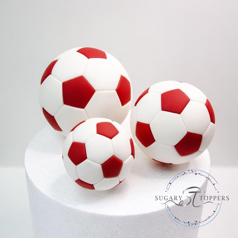 Pu&ograve; includere: Tre decorazioni sferiche per torte a forma di pallone da calcio con un classico motivo a pentagoni bianchi e rossi. Il set comprende un pallone grande e due pi&ugrave; piccoli, tutti con una finitura liscia. &Egrave; visibile il testo SUGARY TOPPERS.