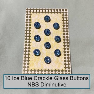 May include: Ten round ice blue crackle glass buttons arranged on a rectangular card with a yellow textured center and a brown and white diamond border. The card features the text 10 Ice Blue Crackle Glass Buttons NBS Diminutive.