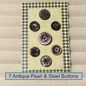 May include: A collection of 7 antique pearl and steel buttons arranged on a rectangular card with a green and white checkered border. The buttons feature intricate metallic and iridescent details in various circular patterns and sizes.