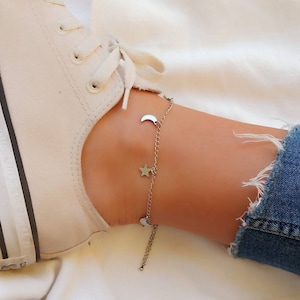 Peut inclure: Un bracelet de cheville argenté avec une chaîne délicate et des breloques en forme d'étoile et de croissant de lune.