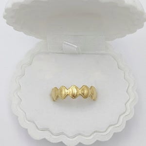 May include: A gold ring featuring a design of multiple seashells. The ring is presented in a white seashell-shaped box.