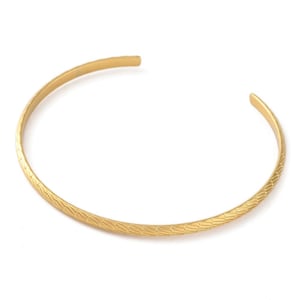 May include: A gold-coloured cuff bracelet with a textured, geometric pattern. The open-ended design allows for easy wear. This jewellery piece is a stylish accessory for everyday wear.