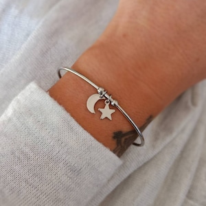 May include: A silver bangle bracelet with a crescent moon and star charm. The bracelet is on a person's wrist.