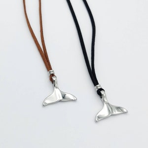 May include: Two necklaces with silver whale tail pendants. One necklace has a brown leather cord and the other has a black leather cord.