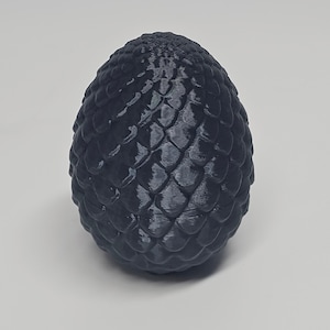 May include: A dark gray, egg-shaped object with a textured, scale-like pattern. The surface has a slightly glossy finish, and the overall shape is smooth and rounded. The object is likely a decorative item or a prop.