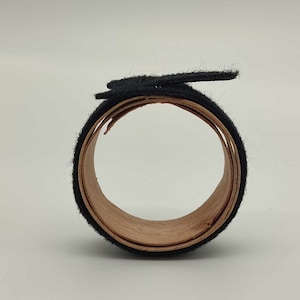 May include: A roll of black felt tape with a wooden core. The tape is rolled up and the end is folded over to secure it.