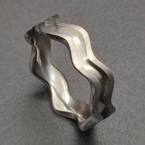 May include: A silver-toned ring with a wavy, textured design. The ring is made of two bands that are intertwined.