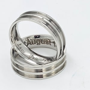 May include: Two silver wedding bands with engraved text. The top band has the text "August 1" and the bottom band has the text "Love you forever".