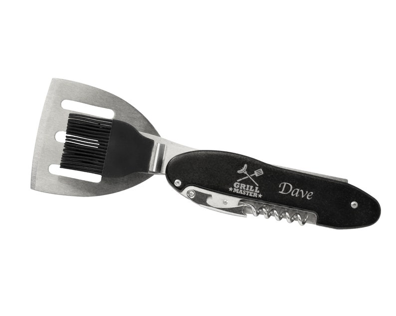 Puede incluir: Un utensilio de cocina multifunci&oacute;n para barbacoa de acero inoxidable y negro. Cuenta con una esp&aacute;tula, un pincel para untar, un sacacorchos y un abridor de botellas. El texto "GRILL MASTER" y el nombre "Dave" est&aacute;n impresos en el mango.
