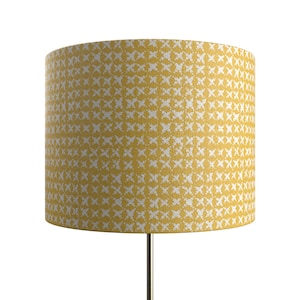 May include: A yellow lampshade with a white geometric pattern. The lampshade is made of fabric and has a cylindrical shape.