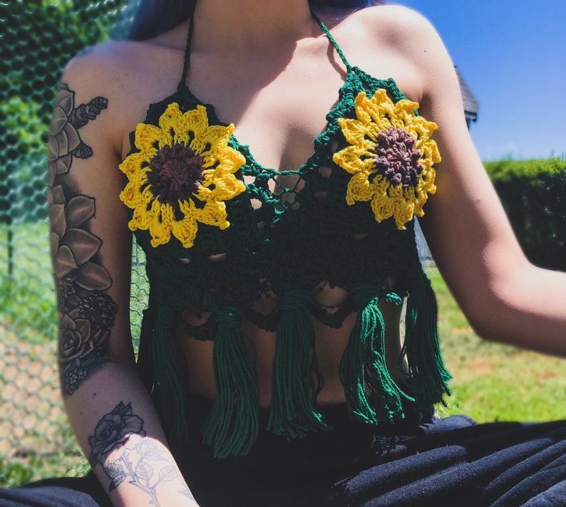 May include: A green crochet halter top with sunflower embellishments and fringe. The top is made of a soft, lightweight yarn and has a relaxed fit.
