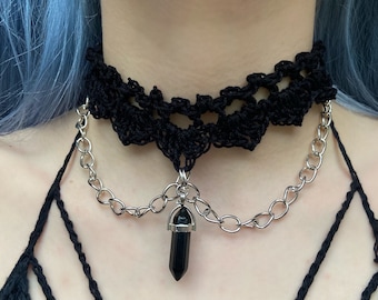 May include: A black crocheted choker necklace with a silver chain and a black crystal pendant.