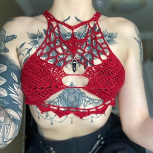 May include: Red crocheted halter top with a spiderweb design and a black crystal pendant.