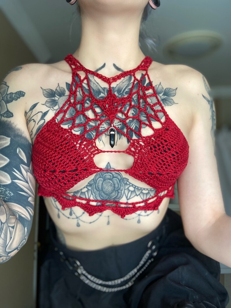 May include: Red crocheted halter top with a spiderweb design and a black crystal pendant.