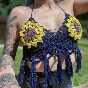 May include: A navy blue crochet top with sunflower-shaped embellishments. The top has fringe detailing and a halter neck style.