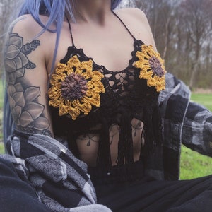 May include: A black crochet top with sunflower-shaped embellishments. The top has a halter style and fringe detailing.
