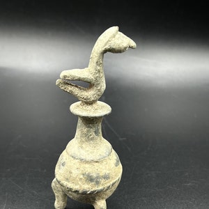 Pode incluir: Um rolha de garrafa de metal cinza com uma base de três pernas e um acabamento em forma de pássaro.