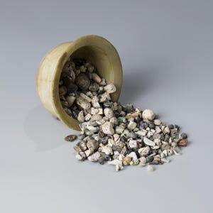 Può includere: Una ciotola arrotondata verde chiaro rovesciata, che versa una collezione di piccole pietre e frammenti di forma irregolare. Le pietre variano di colore, tra cui bianco, grigio e marrone. La ciotola è fatta di un materiale verde chiaro.