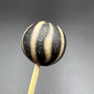 Può includere: Una sfera a strisce bianche e nere su un bastoncino di legno. La sfera è realizzata in un materiale strutturato e ha una finitura lucida.