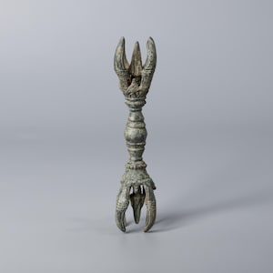 May include: An antique bronze ceremonial object with a claw-like base and a three-pronged top. The object has a detailed, textured design and a long, decorative stem. The background is a solid, neutral grey.