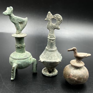 Pode incluir: Três rolhas de garrafa de bronze antigo com designs únicos. Uma apresenta um pássaro estilizado, outra um animal estilizado e a terceira um galo estilizado.