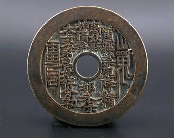 Könnte beinhalten: Eine runde, bronzene chinesische Münze mit aufwendigen chinesischen Schriftzeichen und einem Loch in der Mitte. Die Münze hat einen Durchmesser von etwa 3 cm.