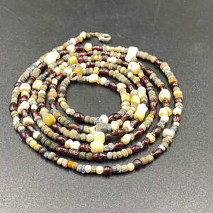 May include: A multi-strand necklace made of various colored beads, including red, white, blue, and brown. The beads are of different sizes and shapes, creating a unique and eclectic look.