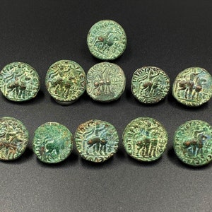Può includere: Dieci monete antiche di bronzo con patina verde, che presentano un disegno di un cavaliere a cavallo. Le monete sono disposte a forma di triangolo su una superficie grigio scuro.