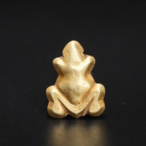 以下が含まれることがあります： 金色のカエルの置物。表面はテクスチャ加工が施されています。カエルは座った姿勢で腕を上げています。置物は黒い背景にあります。