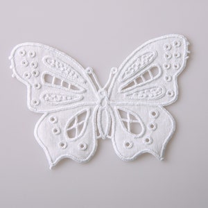 May include: White lace butterfly applique with a delicate design. The butterfly has a cutout pattern and is perfect for adding a touch of elegance to crafts and sewing projects.