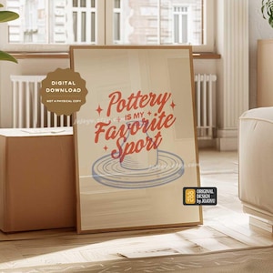 Könnte beinhalten: Ein digitaler Download-Druck mit beigefarbenem Hintergrund, auf dem der Text "Pottery is my favorite sport" in roten und blauen Buchstaben steht. Unter dem Text ist eine stilisierte Illustration einer Töpferscheibe abgebildet. Der Druck ist gerahmt und in einem Wohnzimmer ausgestellt.