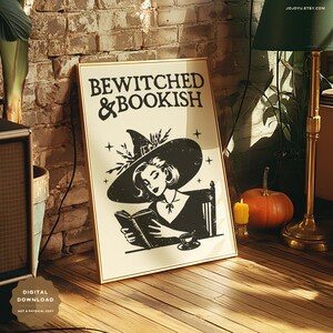 Puede incluir: Una ilustraci&oacute;n en blanco y negro de una bruja leyendo un libro. La bruja lleva un sombrero puntiagudo y un vestido largo. El texto "BEWITCHED & BOOKISH" est&aacute; impreso sobre la bruja.