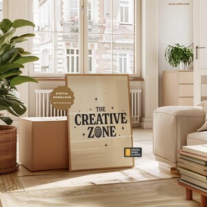 May include: A beige framed print with black text that reads "The Creative Zone" with a stylized swirl design. The print is on a light wood floor in a room with a couch and a window.