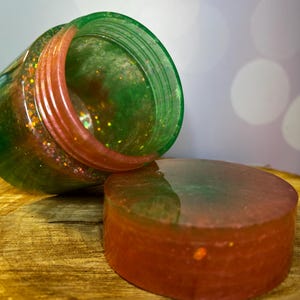 May include: Two round, clear containers with a green and pink swirl design. The containers are filled with glitter and have a shiny finish.