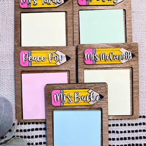 Könnte beinhalten: Fünf Holz-Notizhalter mit Bleistift-Designs und Namen von Lehrern. Jeder Halter hat Platz für eine Haftnotiz. Die Namen sind "Mrs. Tarac", "Mrs. Lashley", "Peace Pop", "Mrs. McConnell" und "Mrs. Burke".