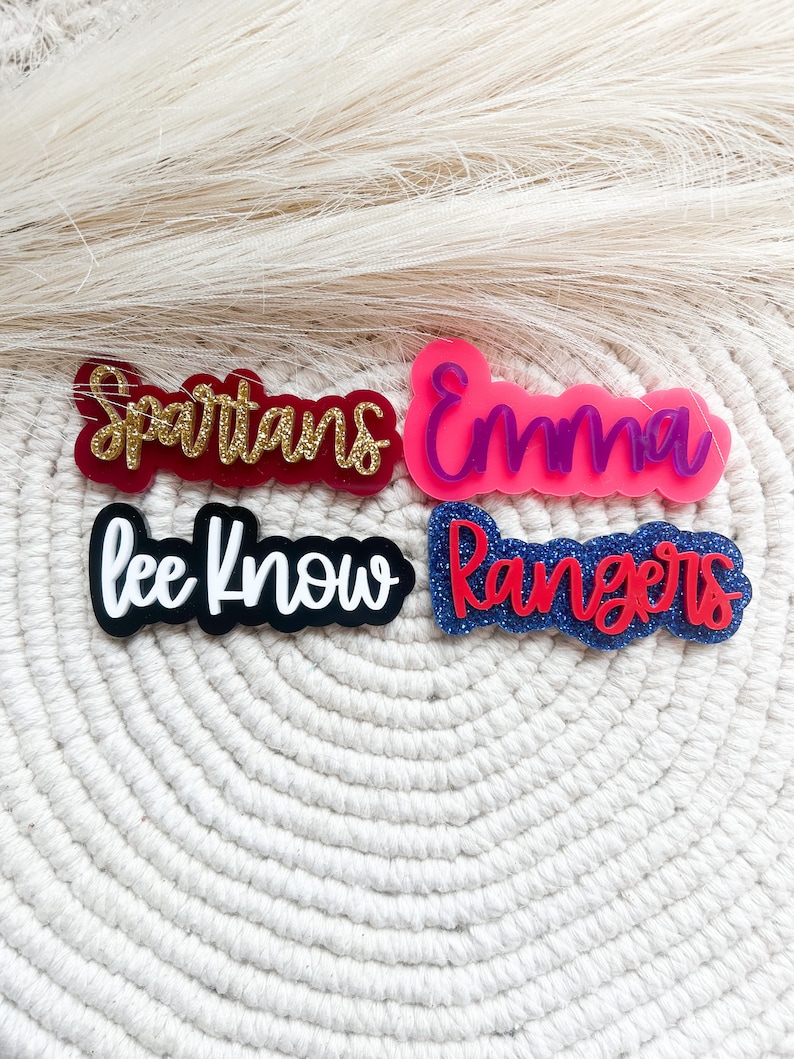 Pu&ograve; includere: Quattro targhette con nome in acrilico con dettagli glitter. I nomi sono "Spartans", "Emma", "Lee Know" e "Rangers".