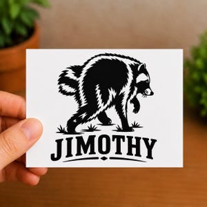 May include: A rectangular white card featuring a black graphic illustration of a raccoon walking through grass. Below the raccoon, the text JIMOTHY is printed in a bold, black, sans-serif font, accented by a small diamond shape and curved lines.