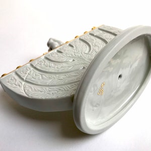 May include: White ceramic menorah with gold accents and a floral design. The base is oval shaped and has a small hole in the center. The menorah is marked with the word "כשר" in Hebrew.