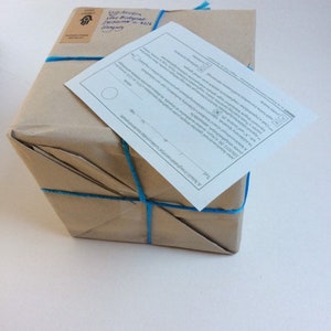 May include: A brown paper package tied with blue string. The package has a white label with text that reads "A Friend's Papery" and a small sticker with a hand symbol.