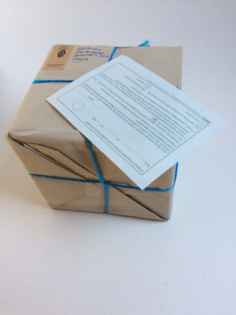 May include: A brown paper package tied with blue string. The package has a white label with text that reads "A Friend's Papery" and a small sticker with a hand symbol.