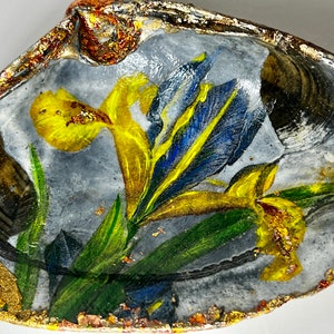 May include: A seashell with a painted design of yellow and blue flowers. The shell is decorated with gold leaf accents.