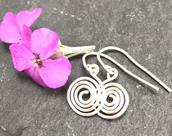 May include: A pair of silver spiral earrings with a simple wire design. The earrings are hanging from a flower.