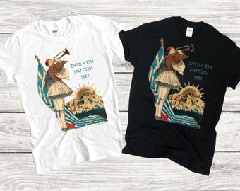 Peut inclure: Deux t-shirts avec un imprimé graphique d'une personne en uniforme militaire tenant une trompette. Le graphique comprend également un drapeau grec, un bâtiment et le texte "ZHTQ H 25H MARTIOY 1821". Un t-shirt est blanc et l'autre est noir.