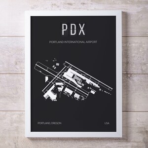 May include: Black and white airport map print with the text "PDX" and "Portland International Airport" in a white box. The map shows the layout of the airport with runways and terminals. The text "Portland, Oregon" and "USA" are at the bottom of the print.