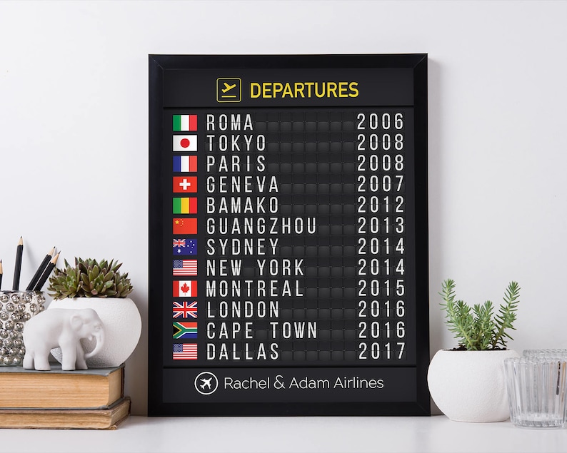 Puede incluir: Un cartel enmarcado en negro con fondo blanco y un tablero de salidas amarillo. El cartel enumera ciudades y a&ntilde;os, incluyendo Roma, Tokio, Par&iacute;s, Ginebra, Bamako, Guangzhou, Sydney, Nueva York, Montreal, Londres, Ciudad del Cabo y Dallas. El cartel tambi&eacute;n incluye un peque&ntilde;o icono de avi&oacute;n y el texto "Rachel & Adam Airlines".